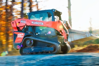 Orange kubota skid steer loader driving on dirt road