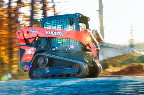 Orange kubota skid steer loader driving on dirt road