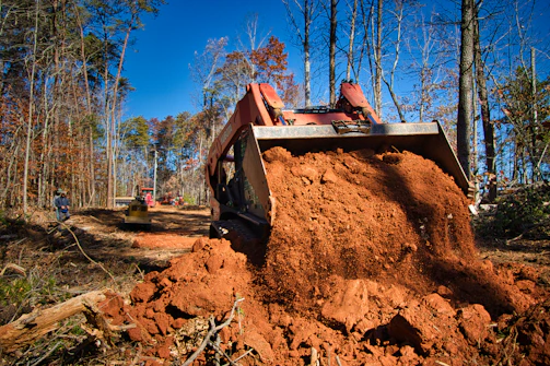 Skid steer loader moving dirt in a wooded area