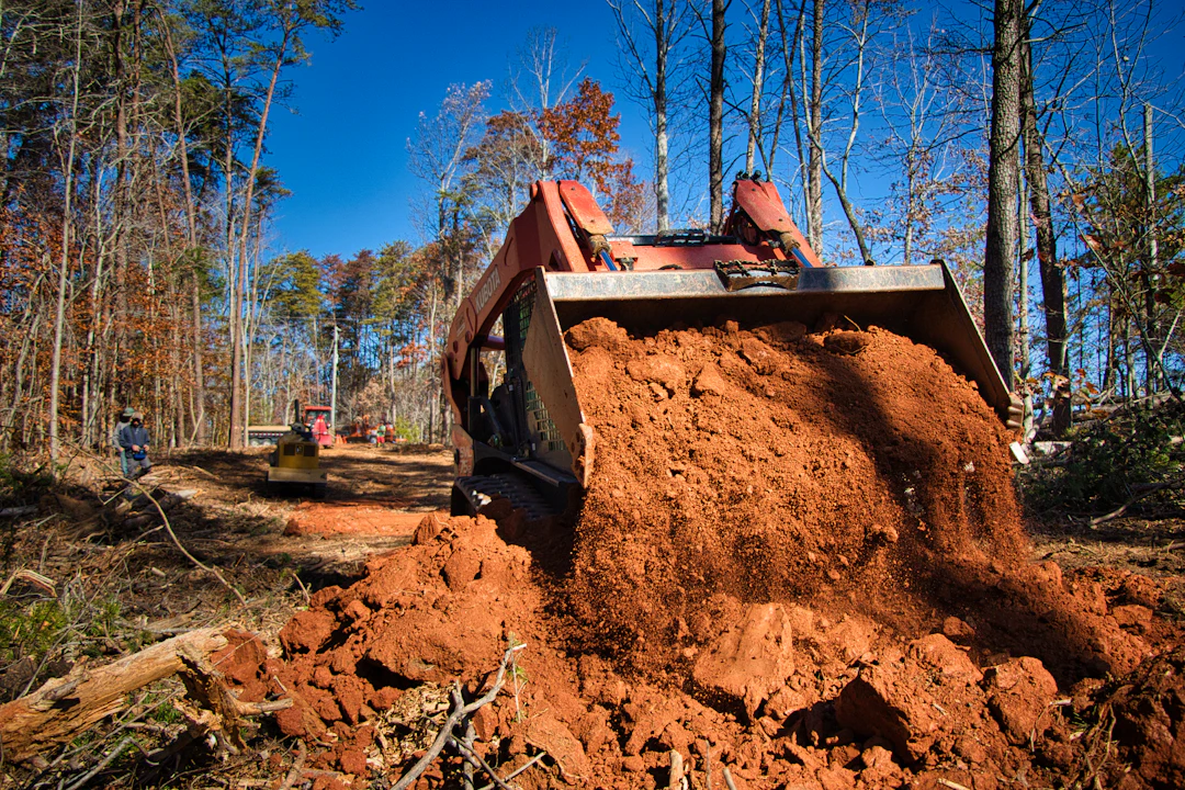 Skid steer loader moving dirt and debris in a partially cleared wooded area