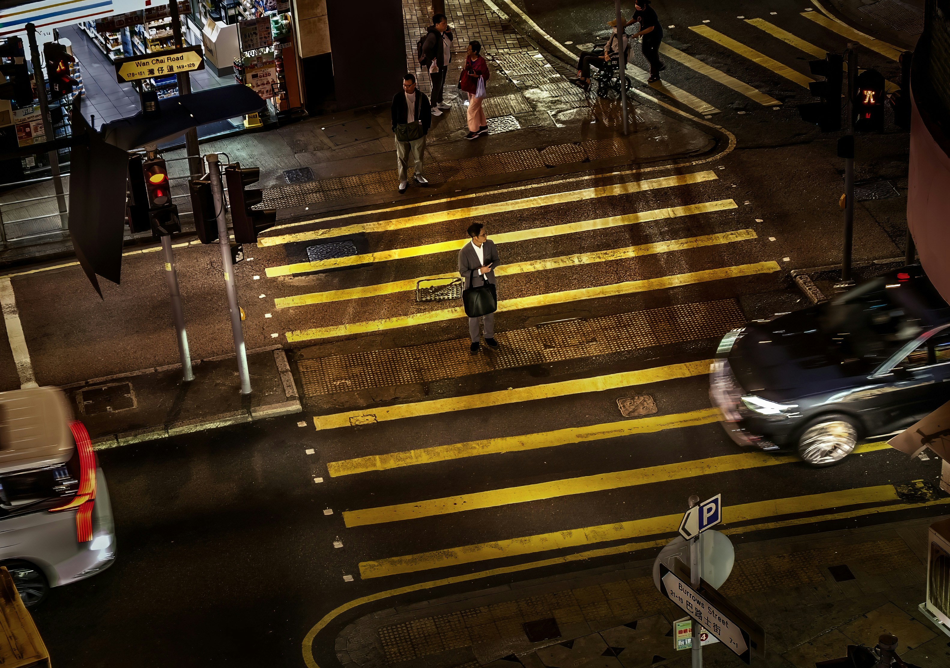 A person crosses a wet city street at night.
