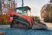 Orange kubota track loader parked on gravel road.