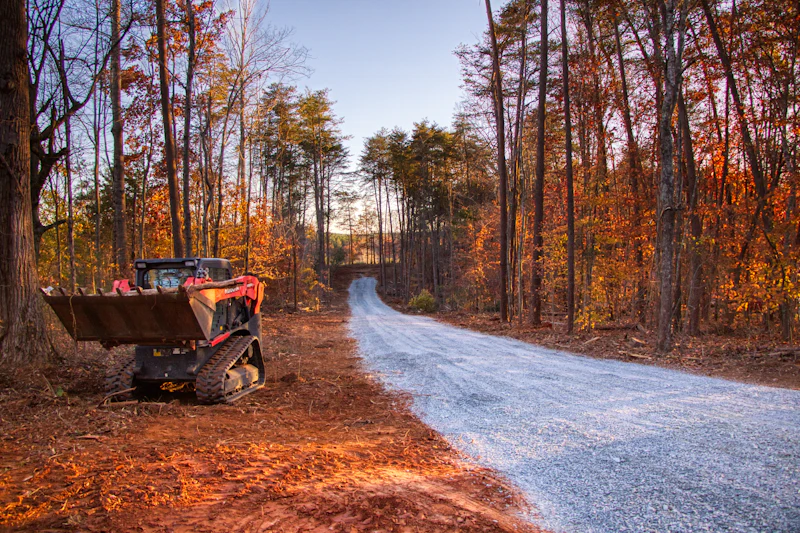 Skid steer on a gravel drive through an autumn forest