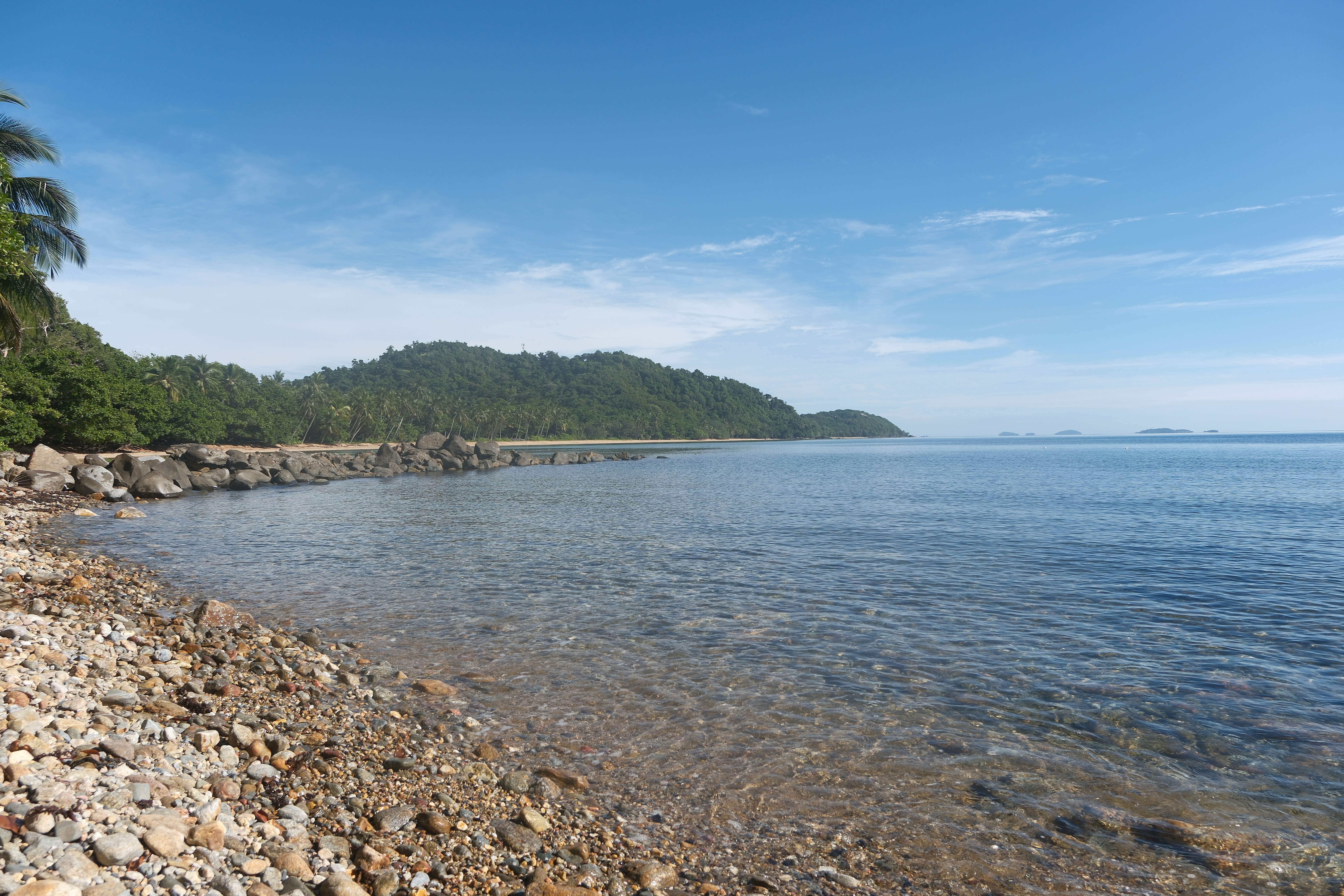 Rocky beach with calm ocean and lush green hills.