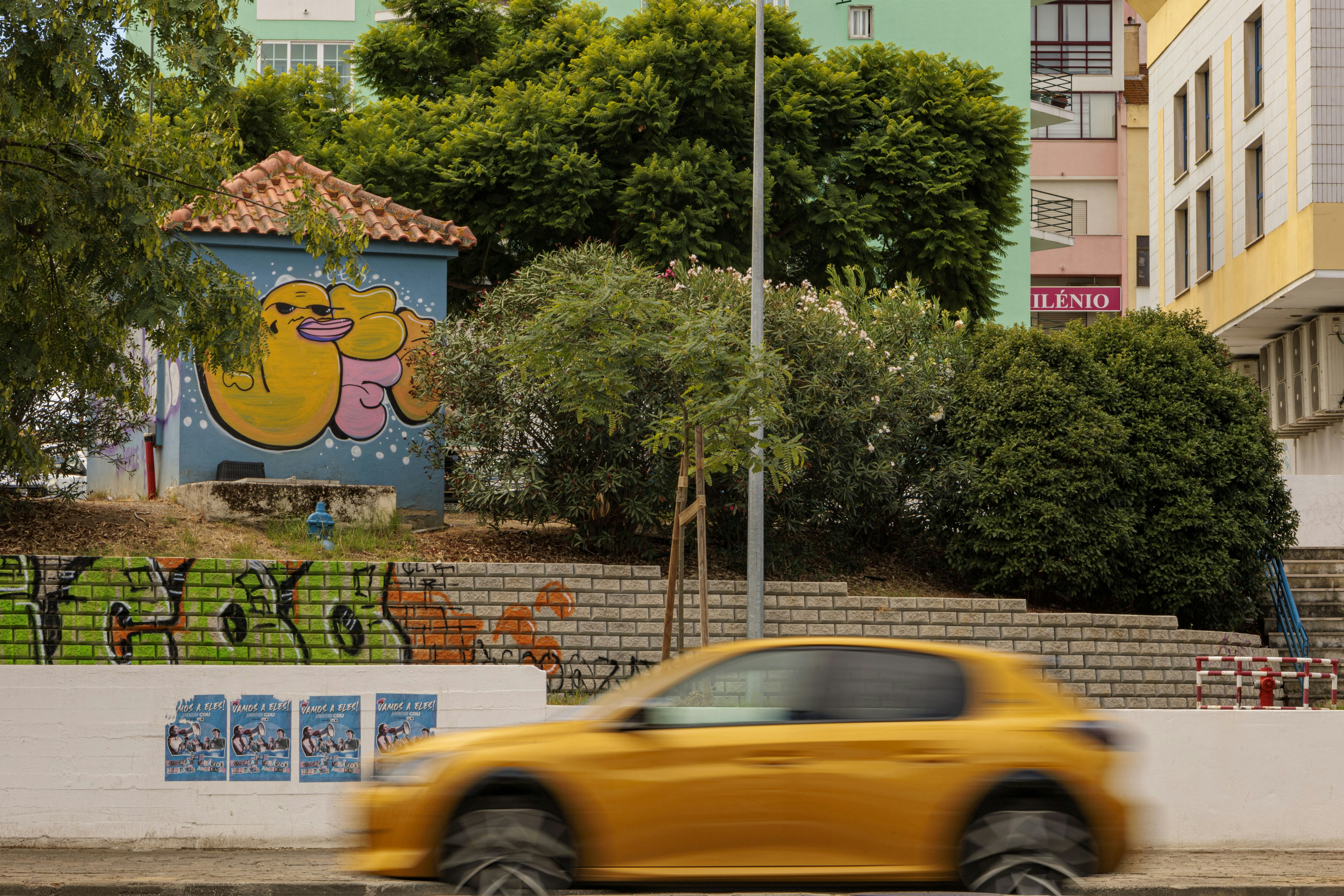Yellow car drives past colorful urban street art.