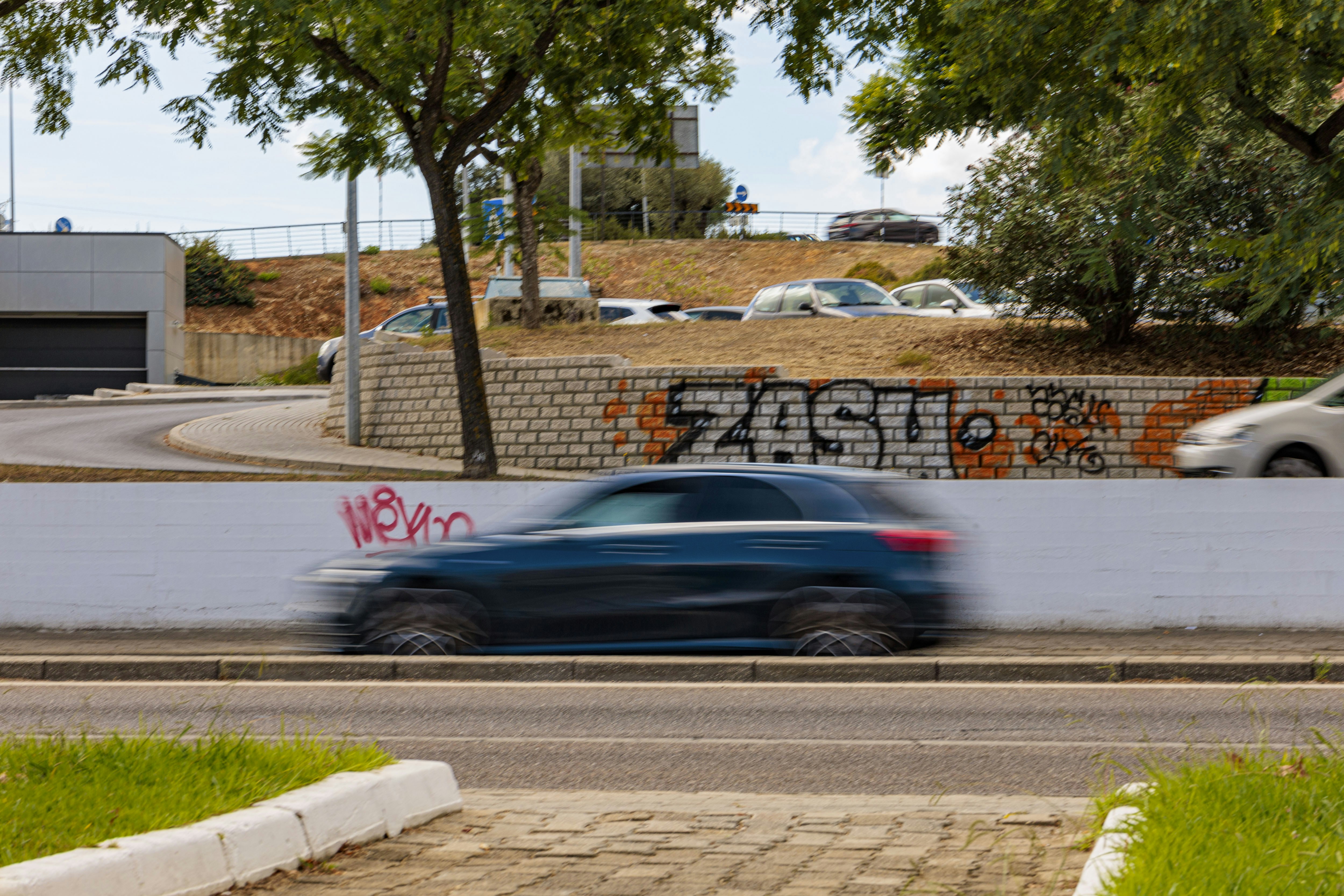 A dark blue car speeds past a graffiti-covered wall.