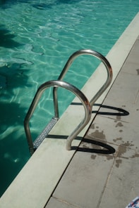 A metal ladder enters a sparkling blue swimming pool.