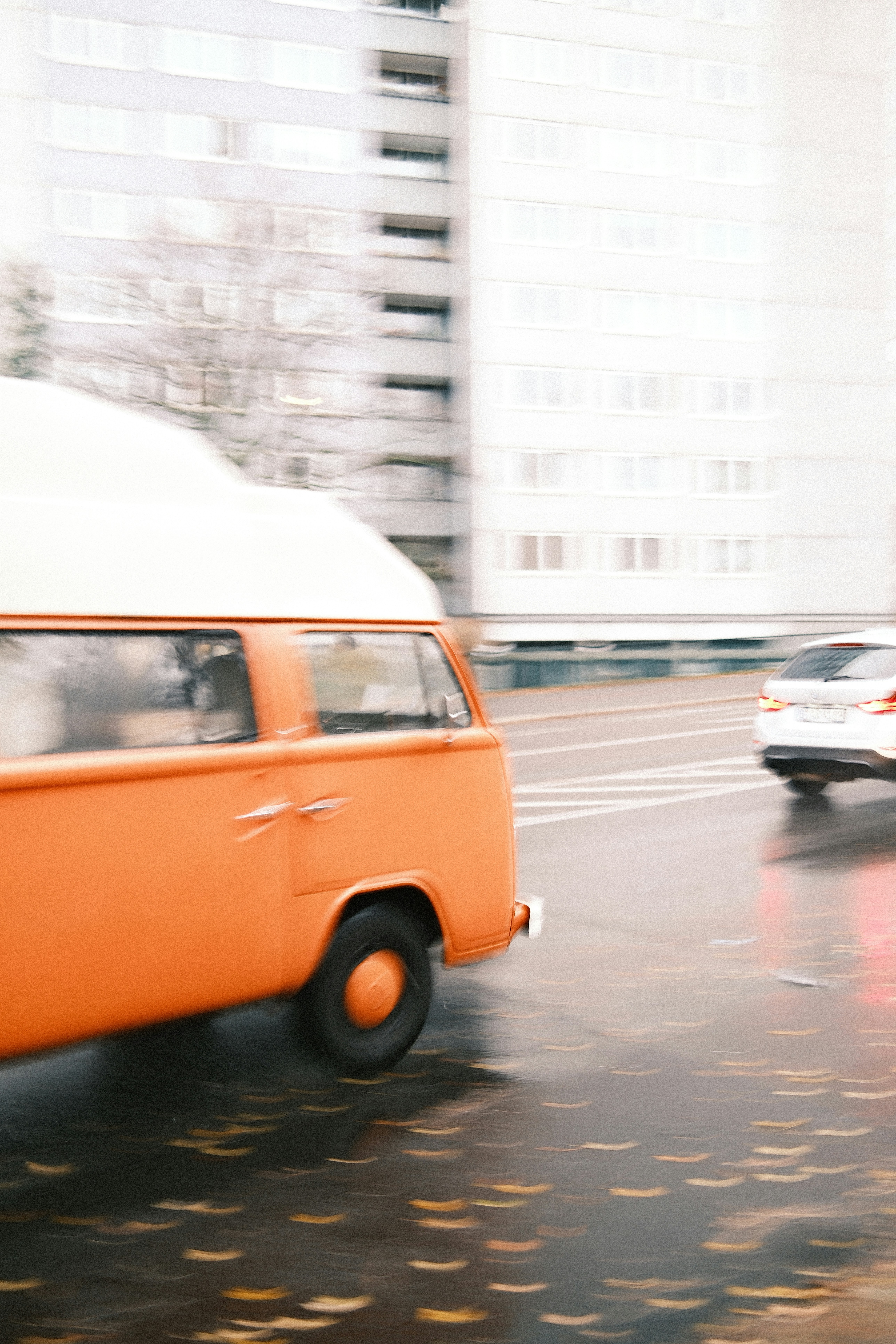 Orange camper van driving on a wet street