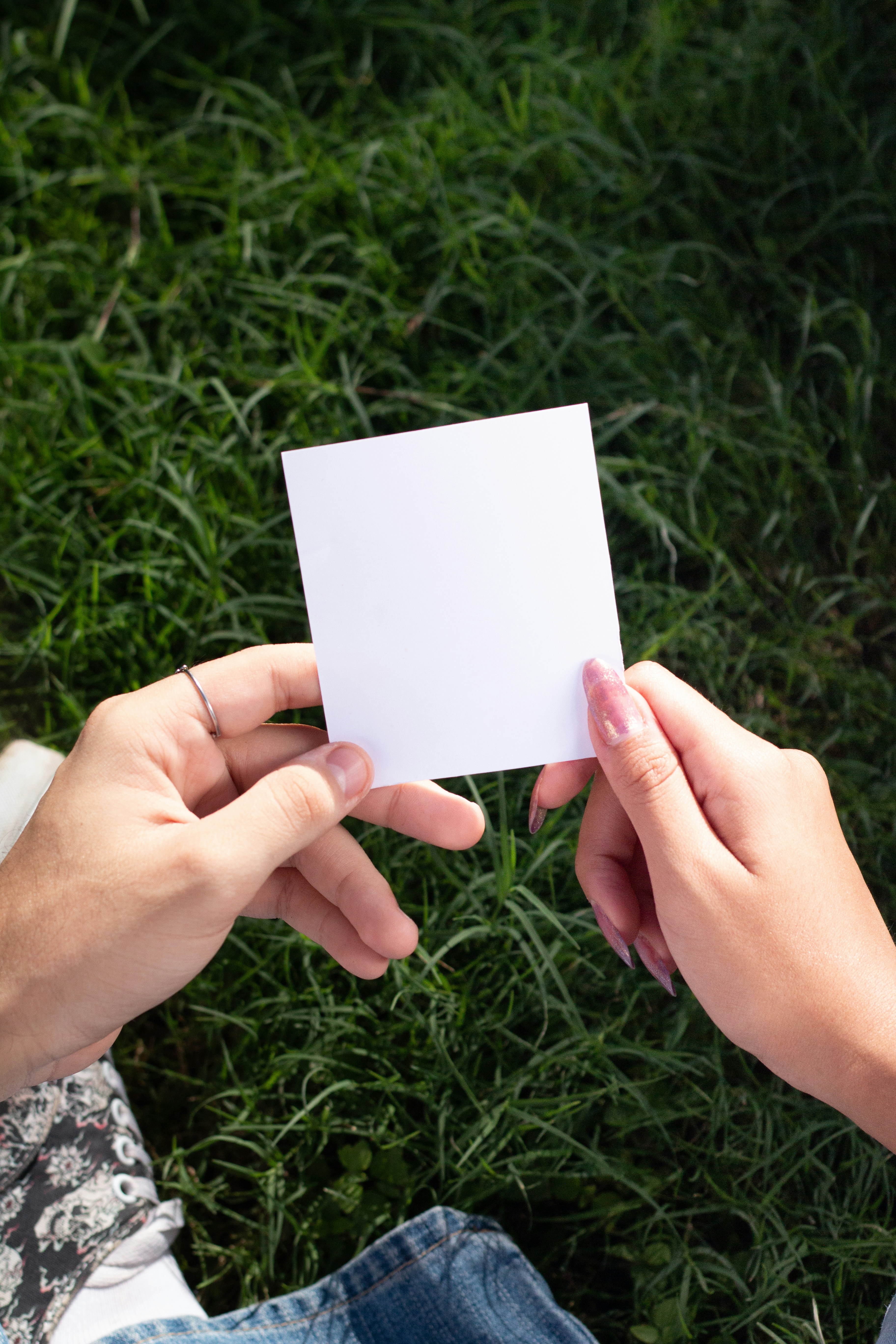 Two hands hold a blank white card on grass