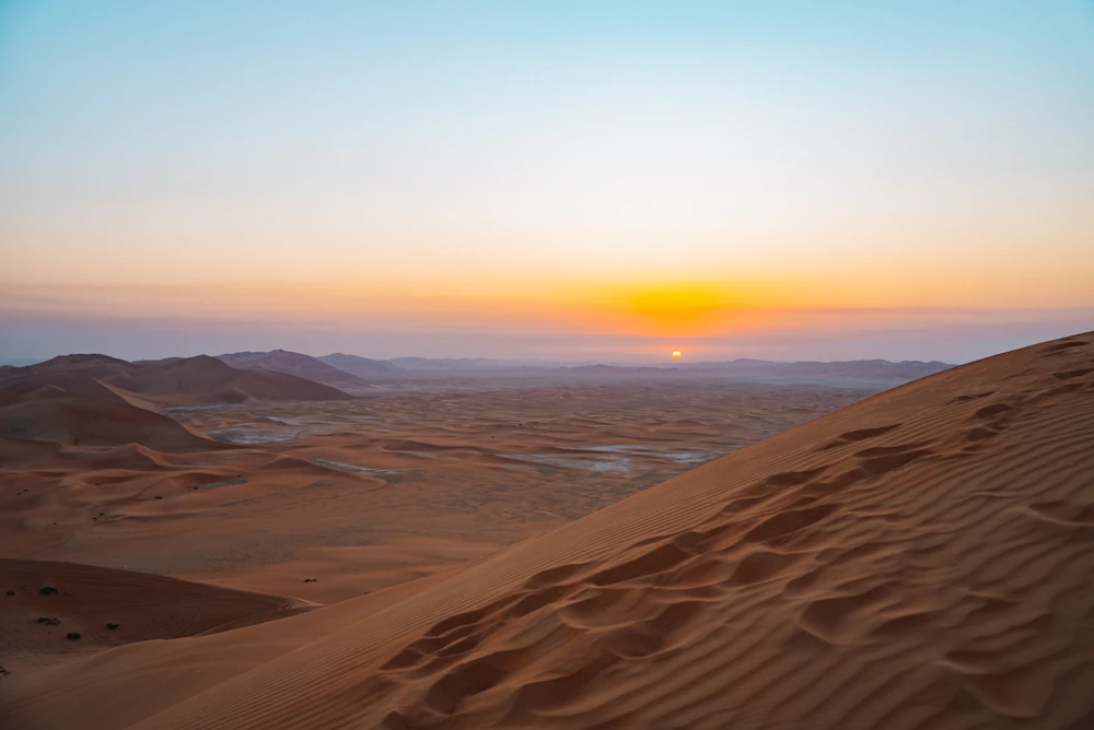 Rippled desert dunes near Dubai under a soft pastel sky as the sun meets the horizon
