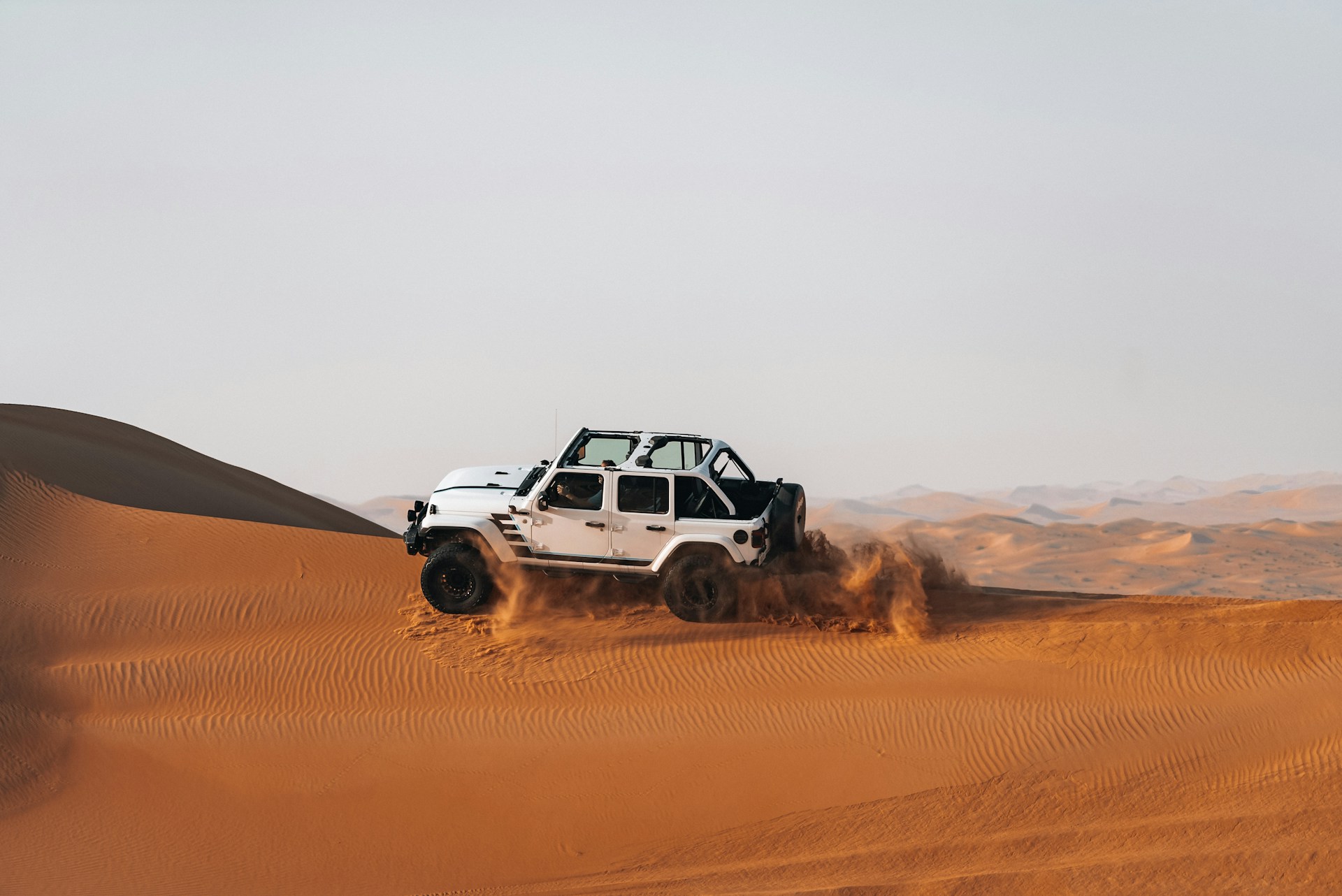 White jeep driving through sandy desert dunes