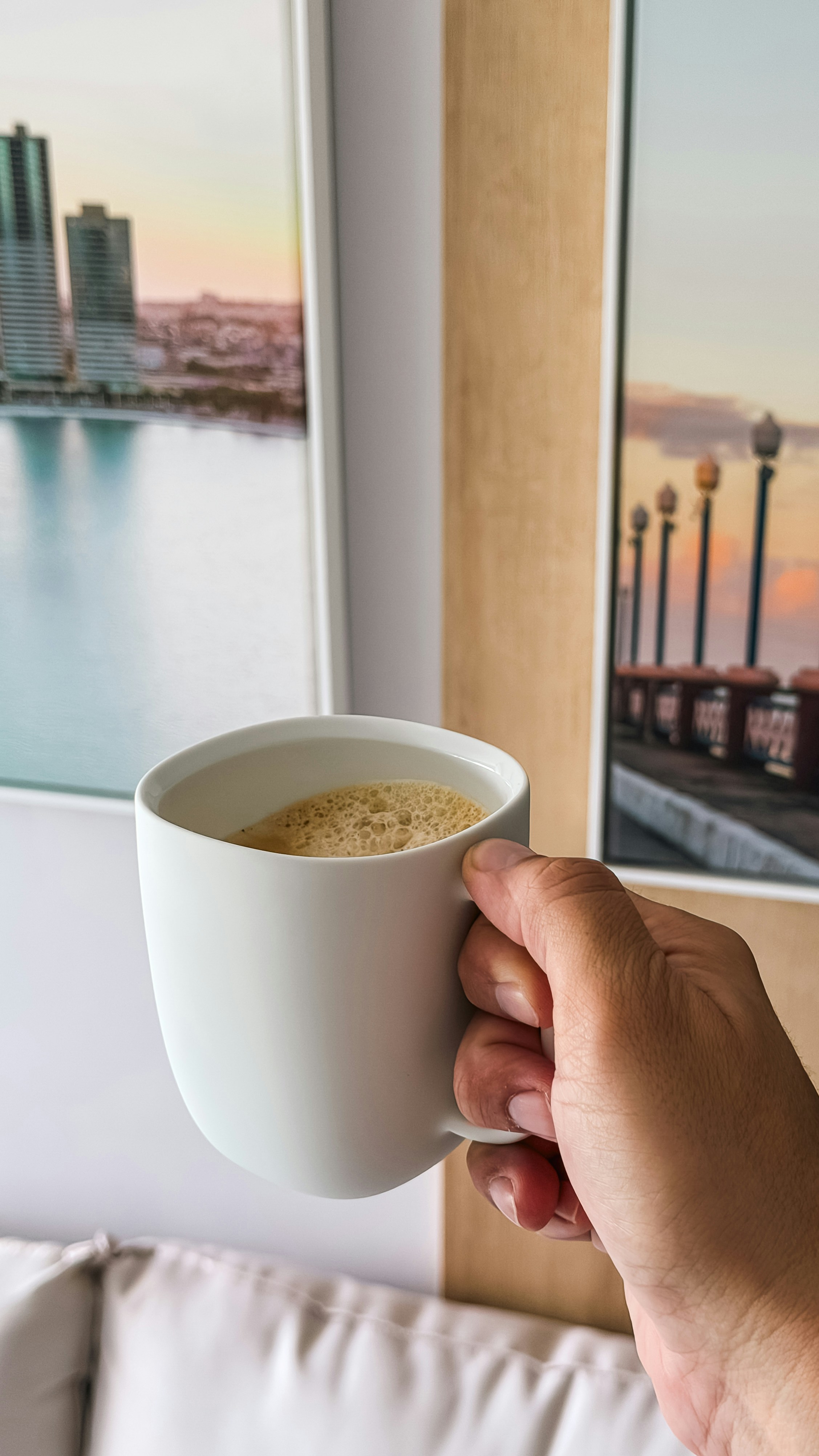 Hand holding a mug of coffee with artwork in background