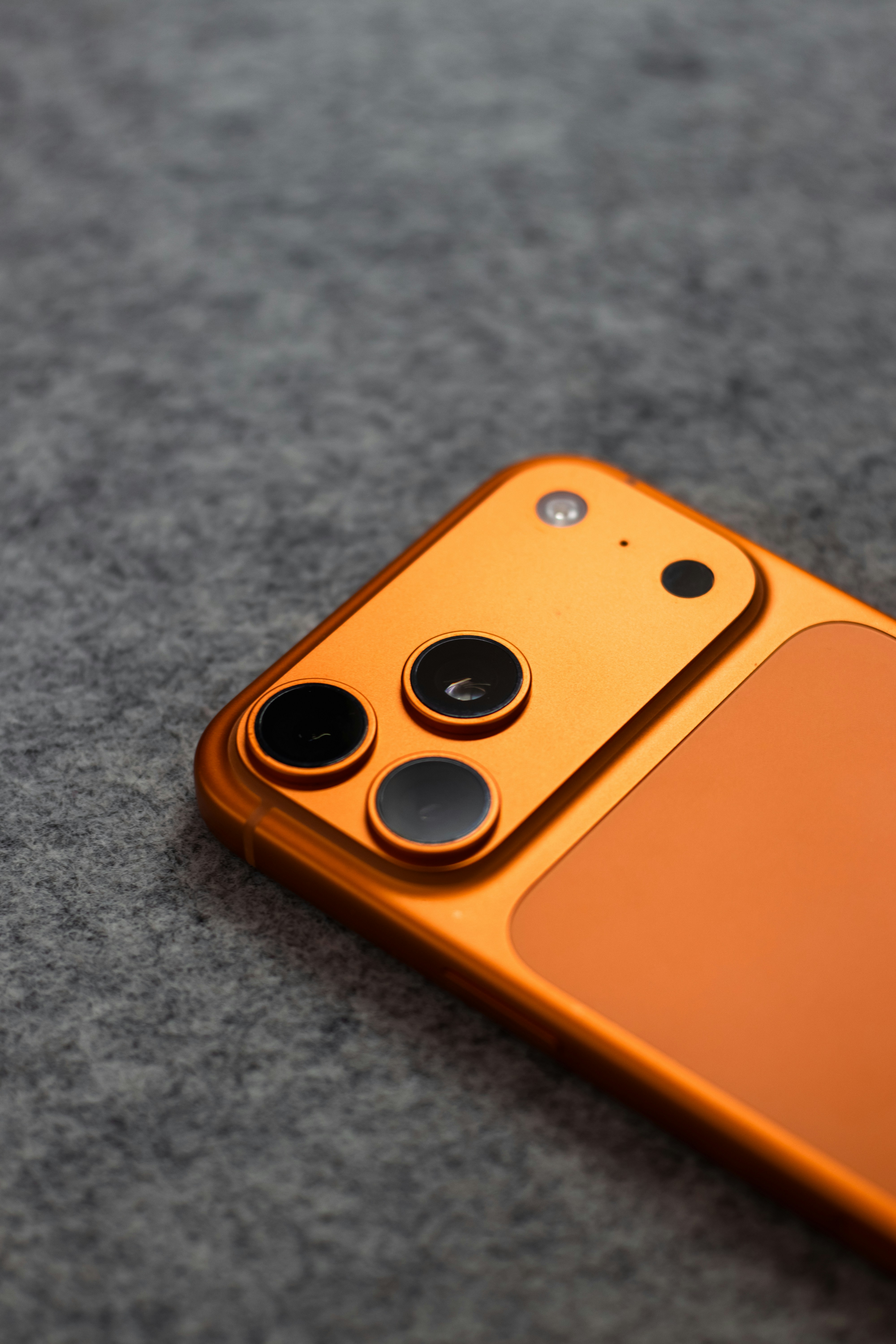 Orange smartphone with triple camera system on gray background.