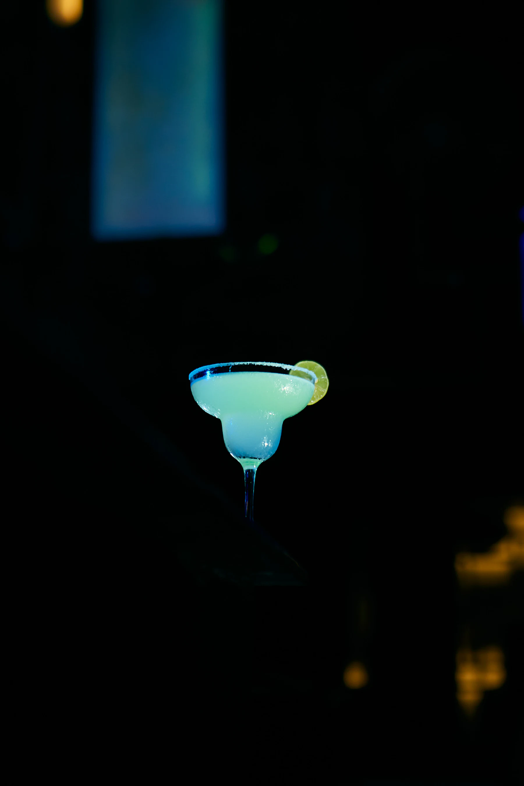 A pale blue margarita in a salt rimmed glass with a lime wedge
