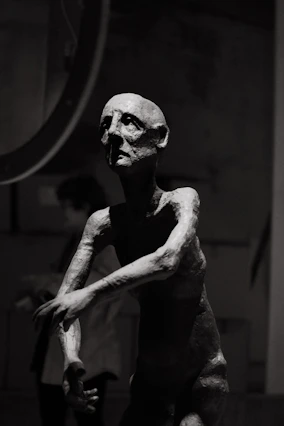 A dark, moody sculpture of a gaunt human figure.