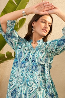 Woman in a blue paisley print dress with arms raised.