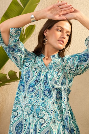 Woman in a blue paisley print dress with arms raised.