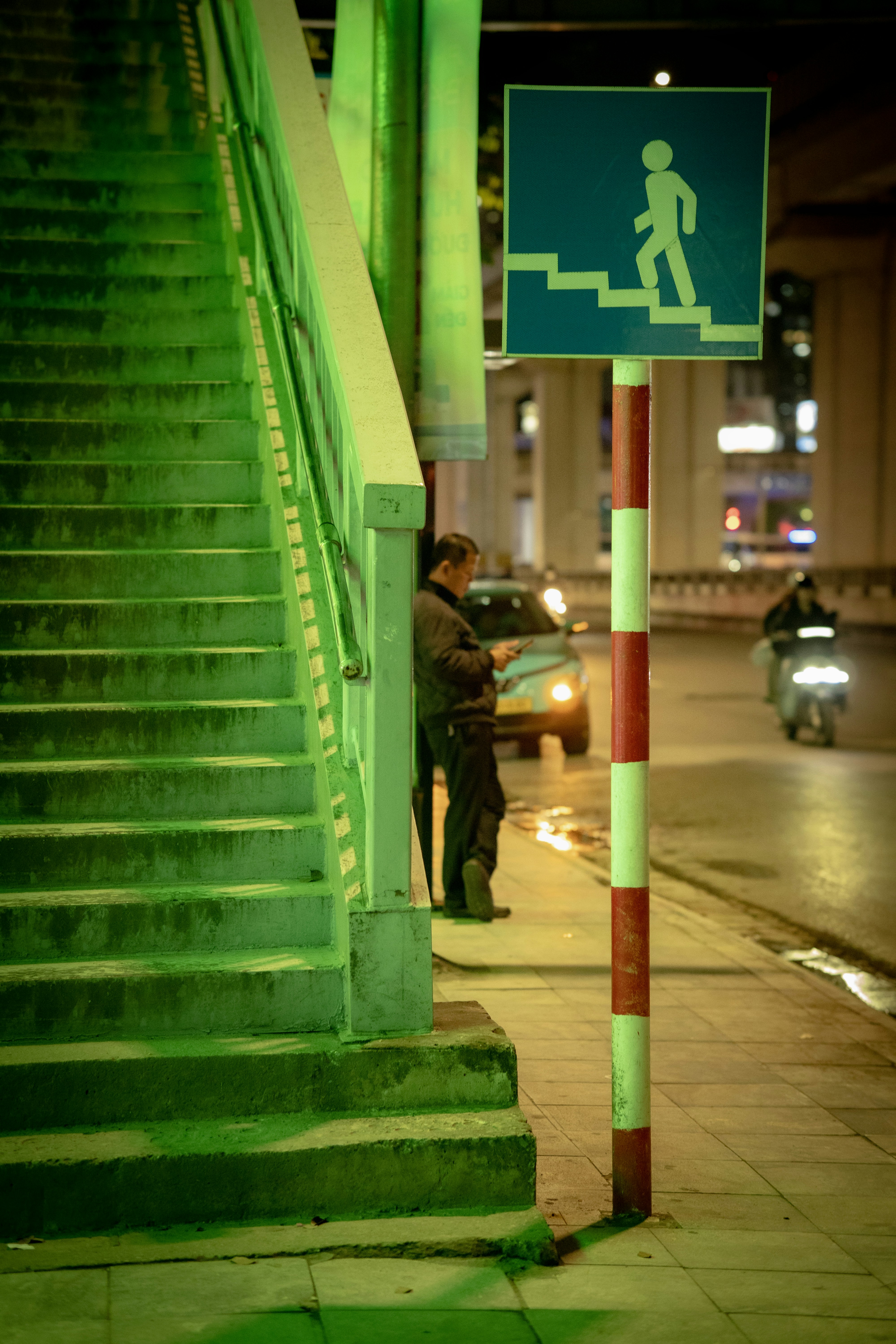 Man standing by green stairs and pedestrian crossing sign