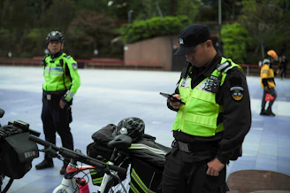 Two security guards with bicycles check their phones.