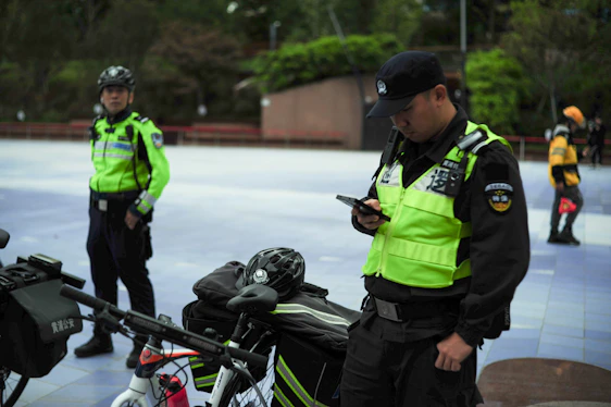 Two security guards with bicycles check their phones.