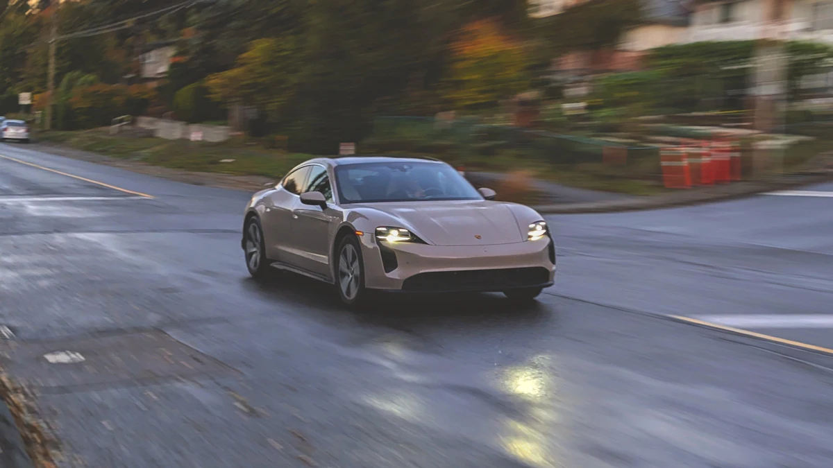 Beigefarbener Porsche Taycan fährt auf einer nassen Straße