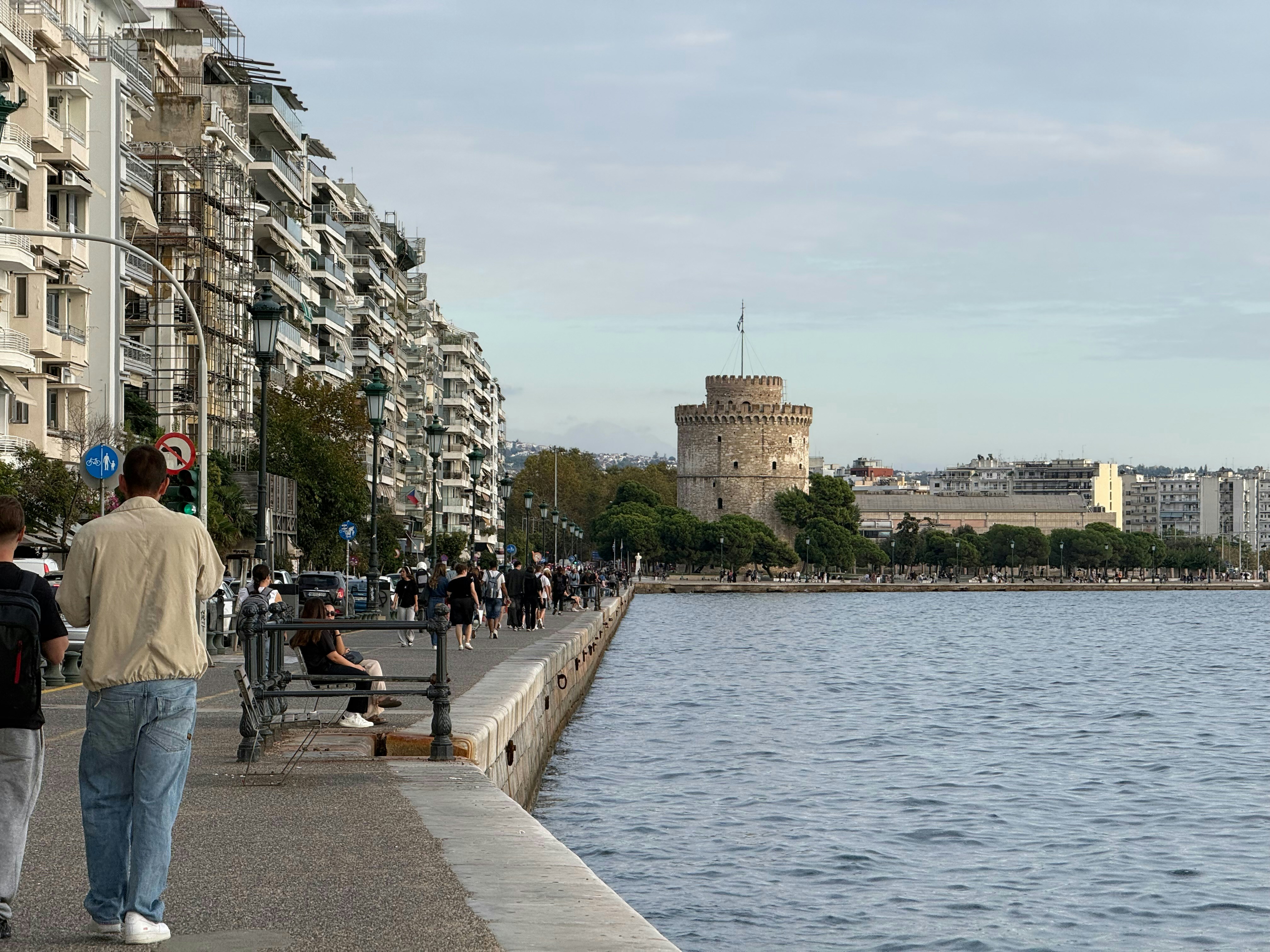 Menschen, die entlang der Wasserpromenade mit weißem Turm spazieren gehen.