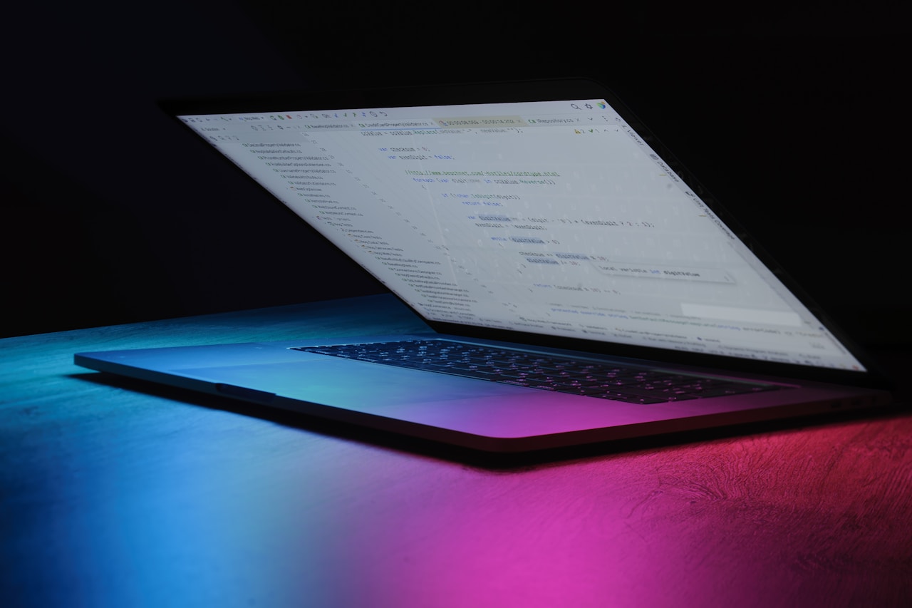 Open laptop showing an IDE code editor with magenta and blue neon glow underneath — visual allegory for the agentic developer workflow on Antigravity 2.0 with Gemini 3.5 Flash