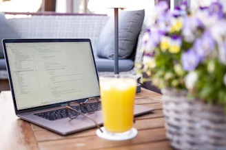 Laptop, drink, and flowers on a wooden table.