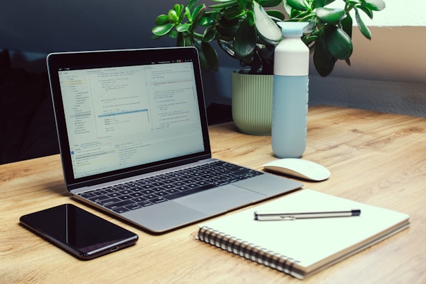 Laptop, phone, notebook, and water bottle on desk.
