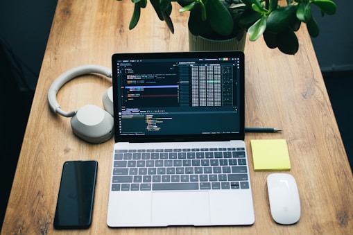 Laptop with code, headphones, phone, and mouse on desk.