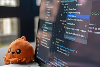 A cute octopus toy sits beside a laptop displaying code.