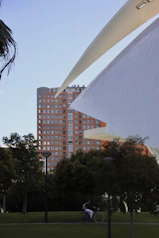 Building and park with a cyclist on a path.