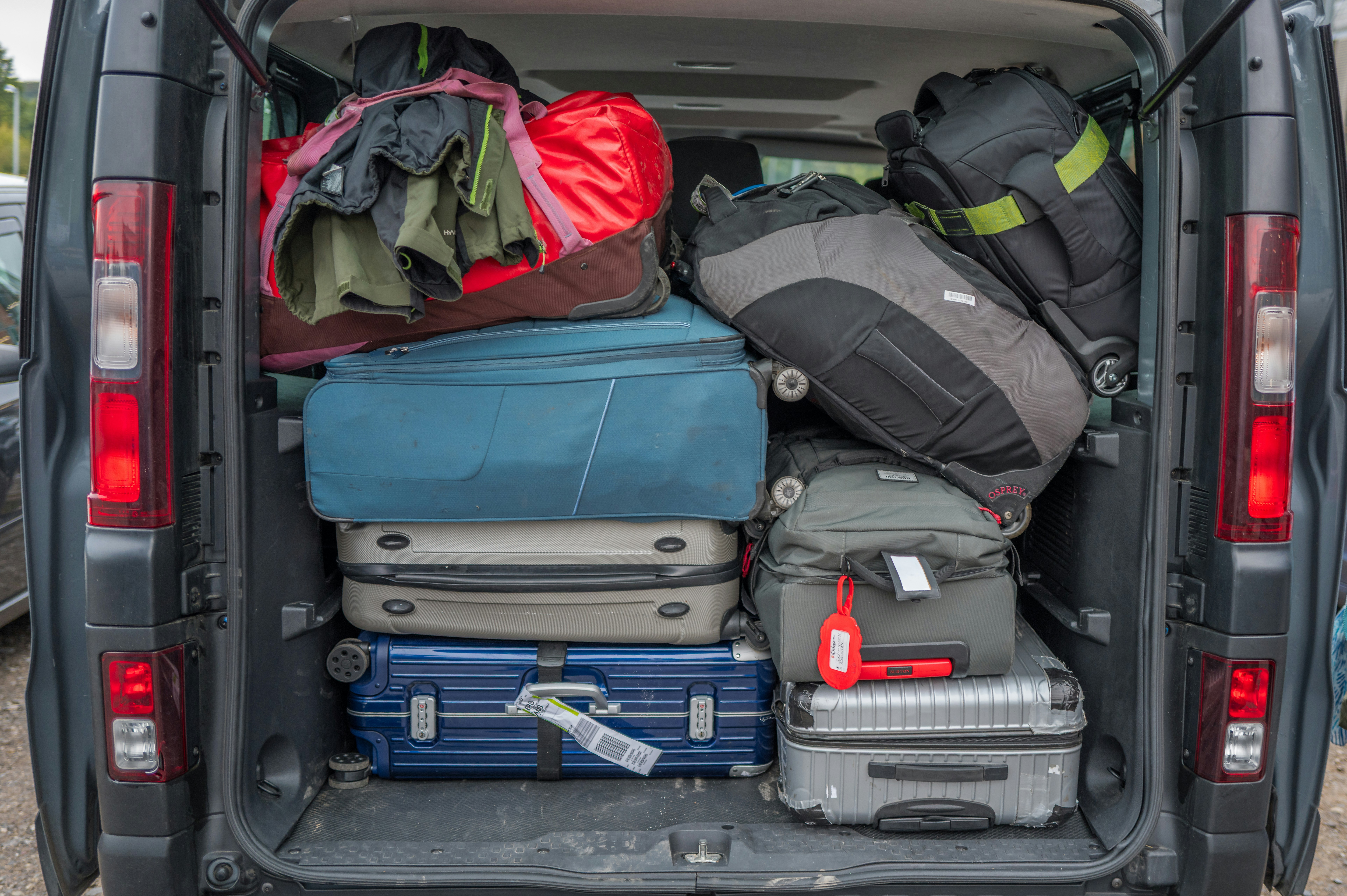 The image depicts the interior of a van's trunk, overflowing with a collection of travel gear. Suitcases, duffel bags, backpacks, and other items are tightly packed, suggesting a trip is imminent. The scene conveys a feeling of excitement and anticipation for a journey.