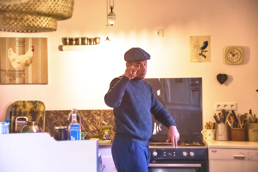 Middle-aged man in a flat cap standing in a home kitchen.