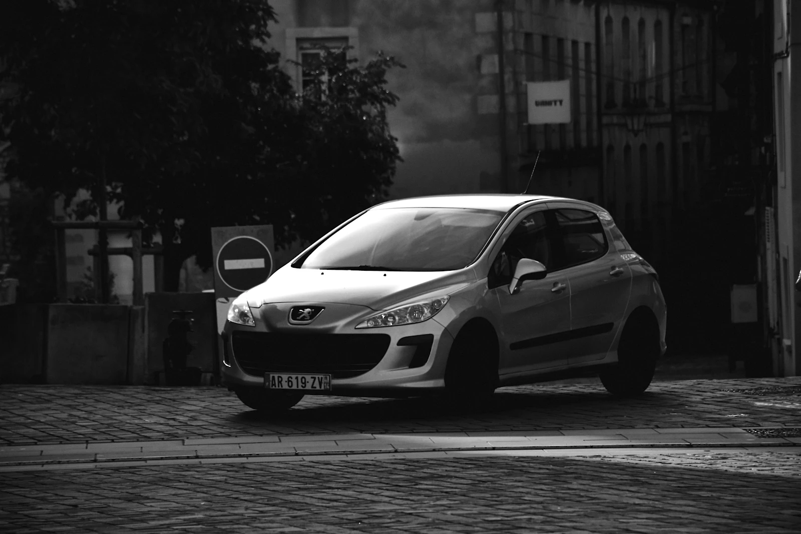Silver Peugeot 308 hatchback parked on a cobblestone street, front three-quarter view