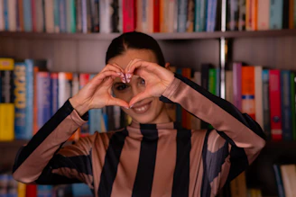 Woman making heart shape with hands in front of bookshelf