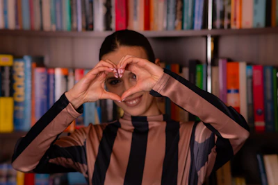 Woman making heart shape with hands in front of bookshelf