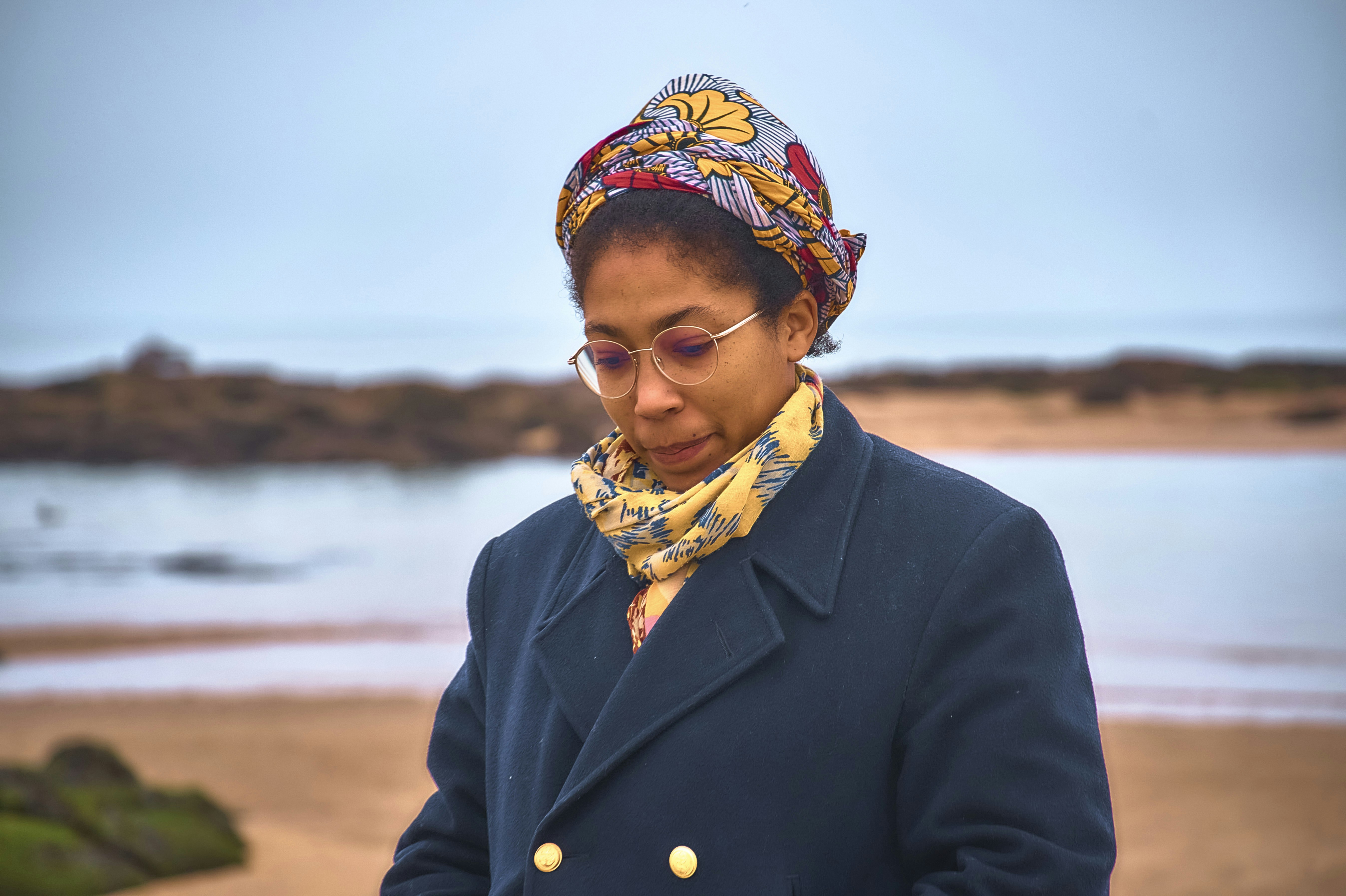 Woman wearing a headscarf and coat at the beach.