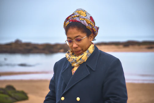 Woman wearing a headscarf and coat at the beach.