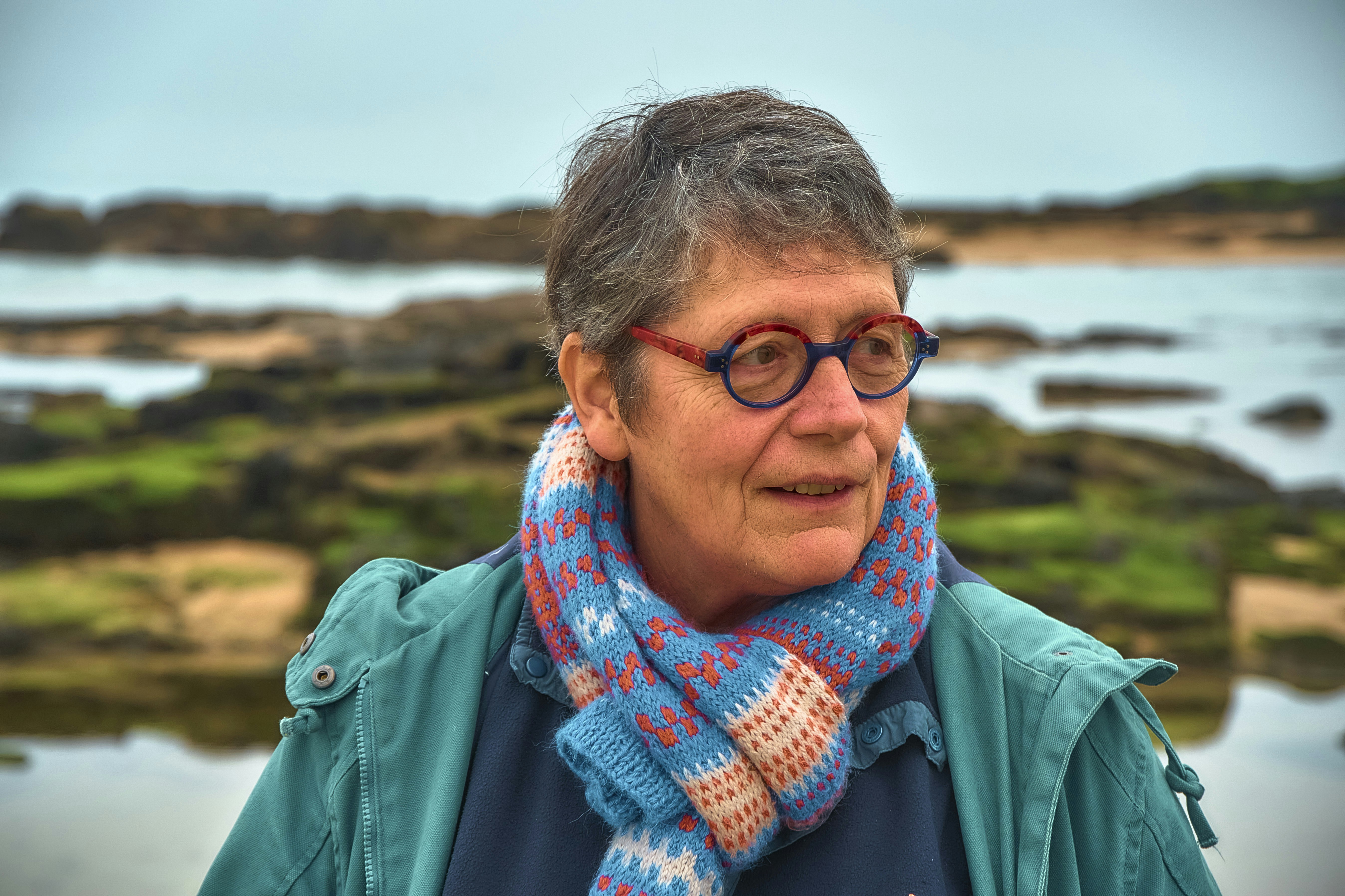 Elderly woman with glasses and scarf by the sea