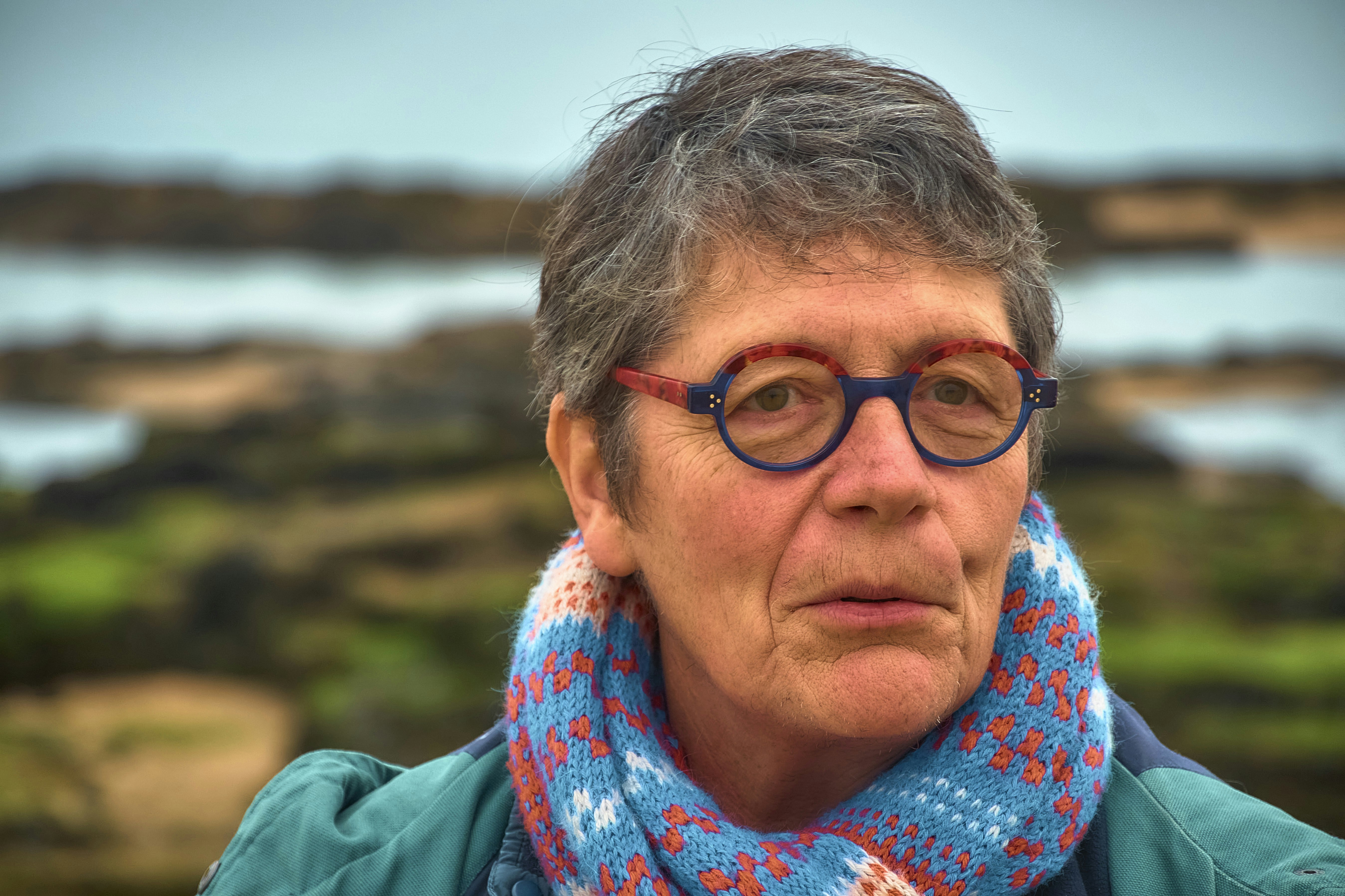 Senhora idosa de óculos e cachecol à beira-mar