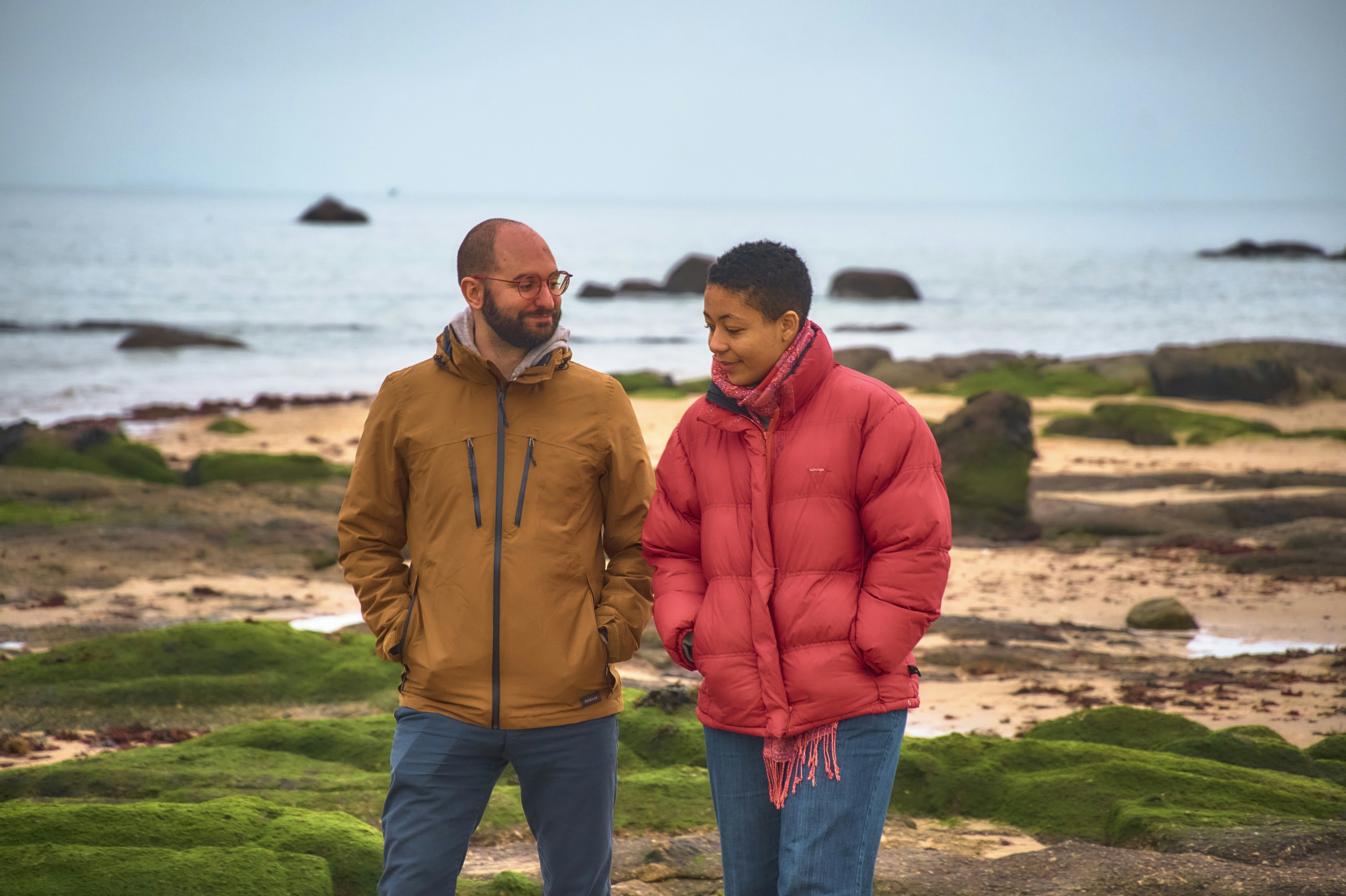 Couple walking on a rocky beach by the sea.
