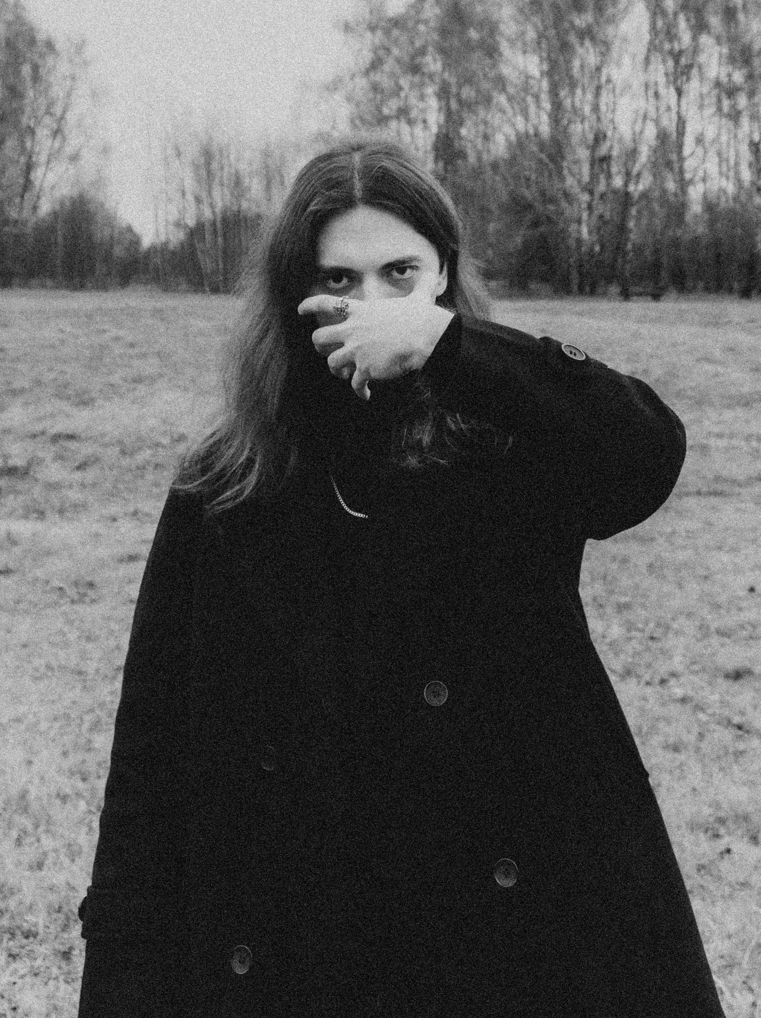 Woman in dark coat covers mouth in field