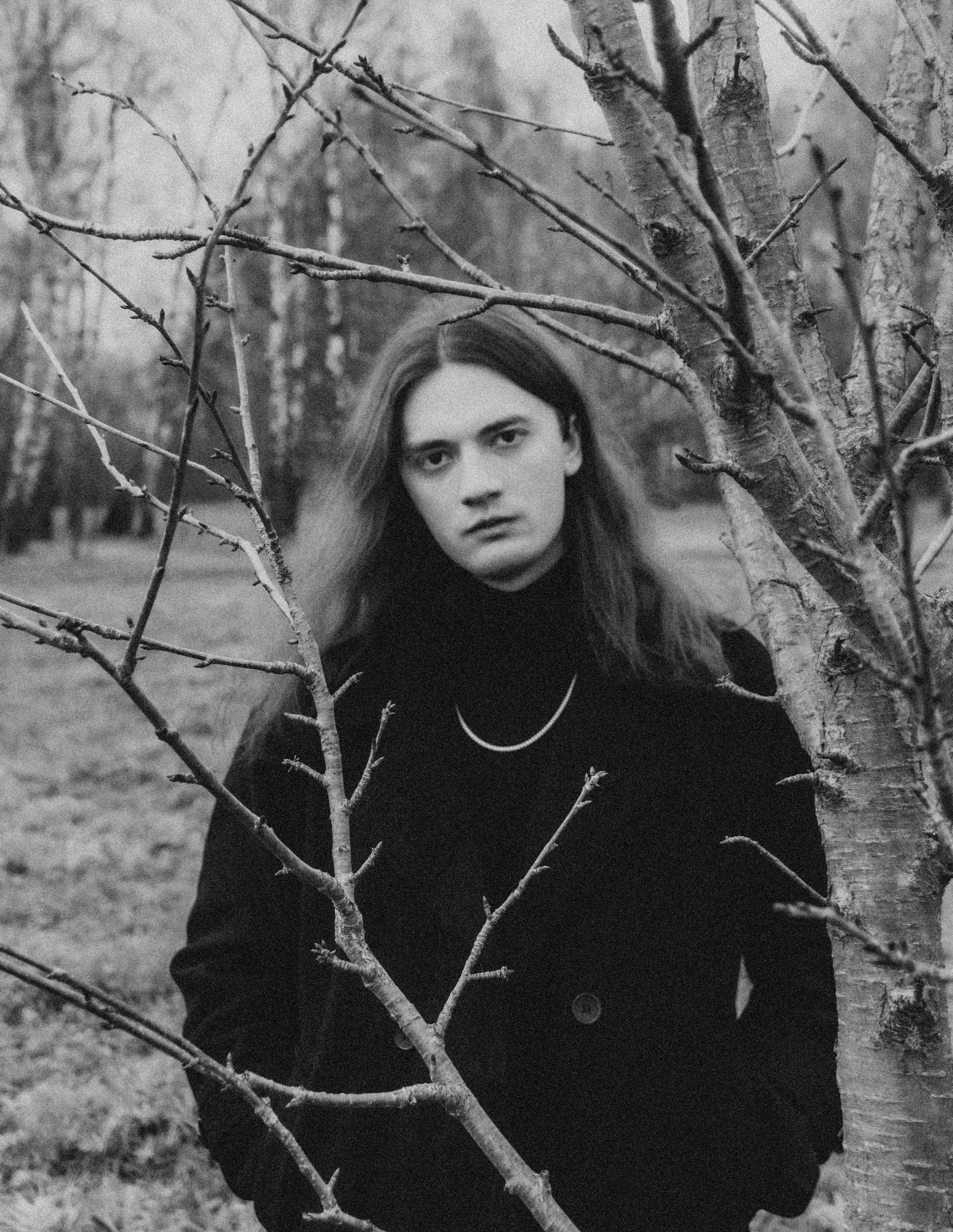 Young man with long hair in a dark coat outdoors.