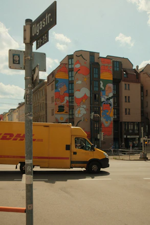 Yellow dhl truck passes building with mural