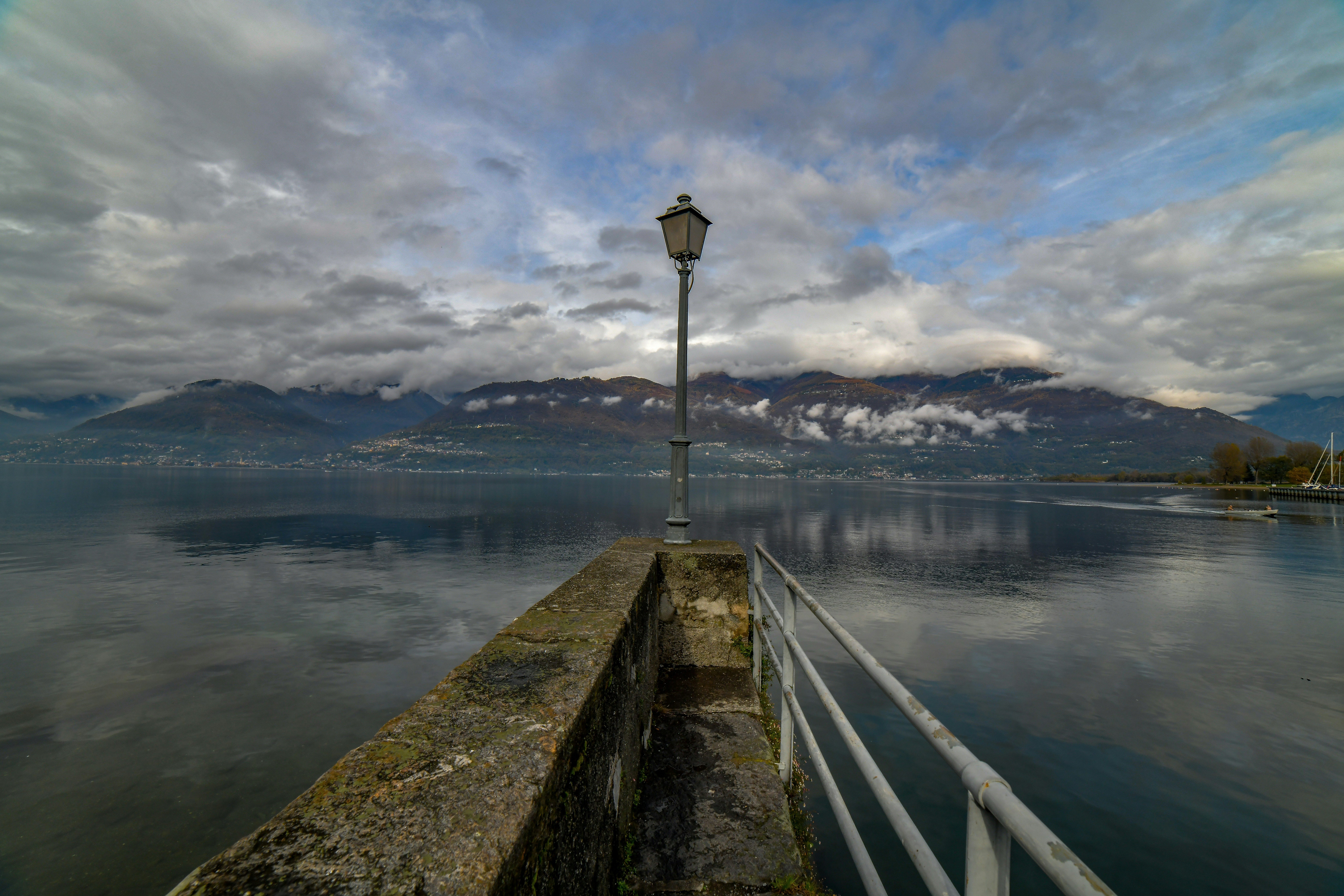 Pier with lamp post overlooking a calm lake and mountains.