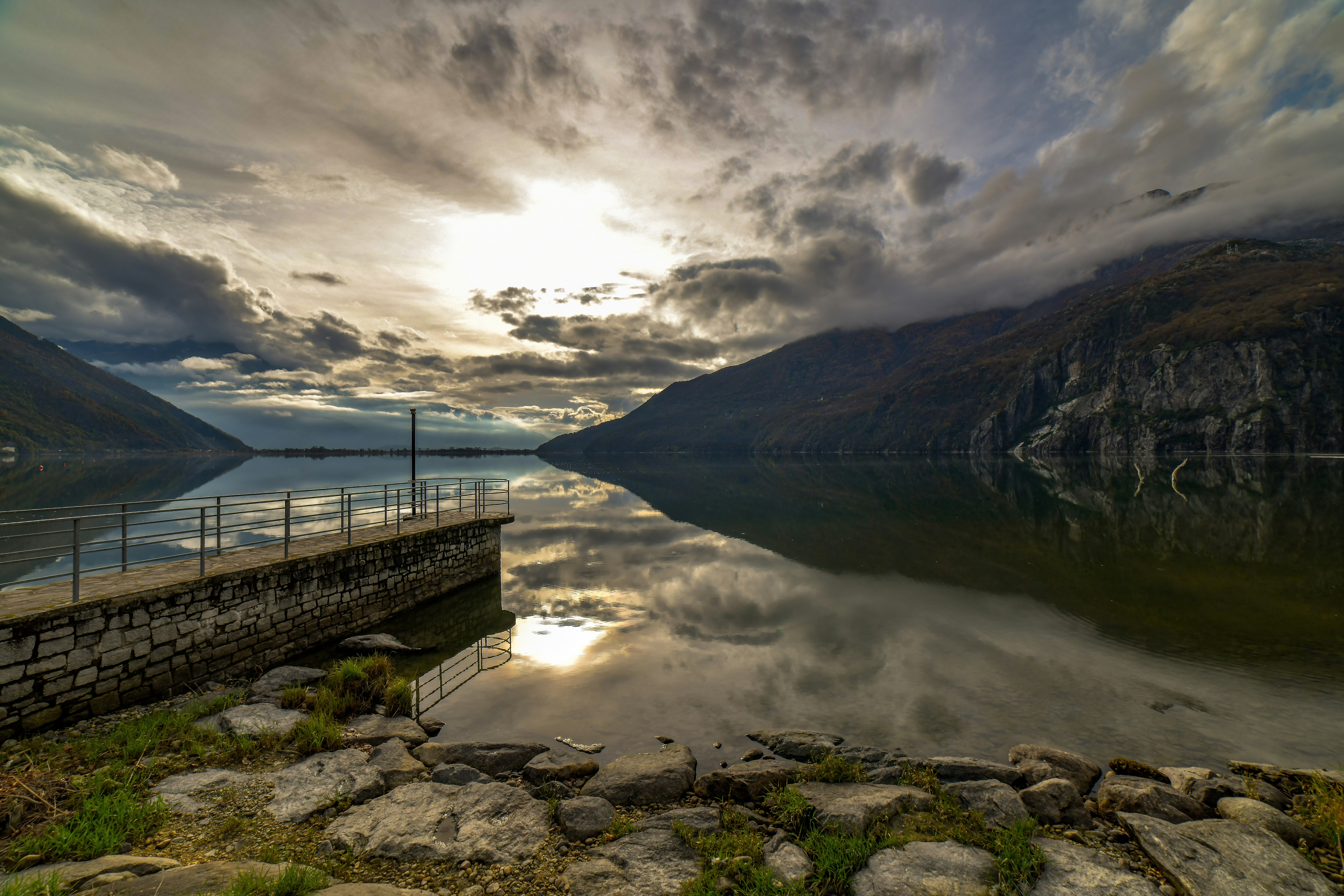Calm lake reflects dramatic cloudy sky and mountains.