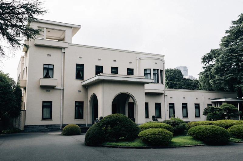 A large white building with manicured bushes in front.