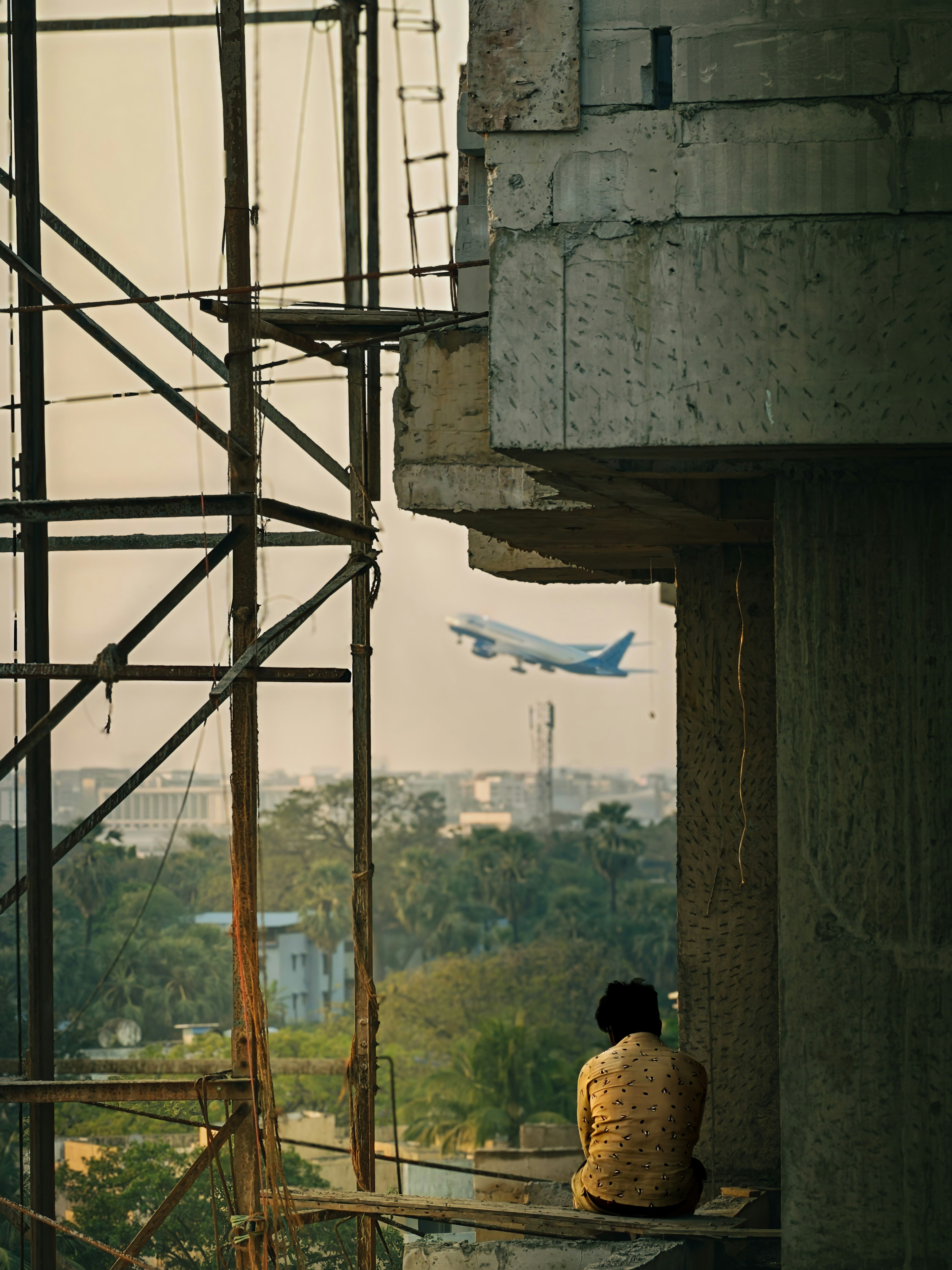 Worker watches plane fly over construction site.