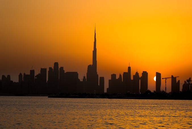 City skyline silhouette against a vibrant sunset over water.